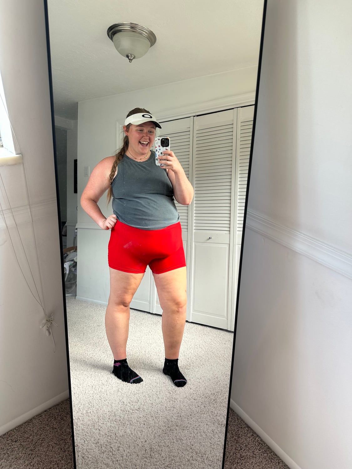 Bailee laughing in a workout mirror, wearing a gray top and bright red shorts